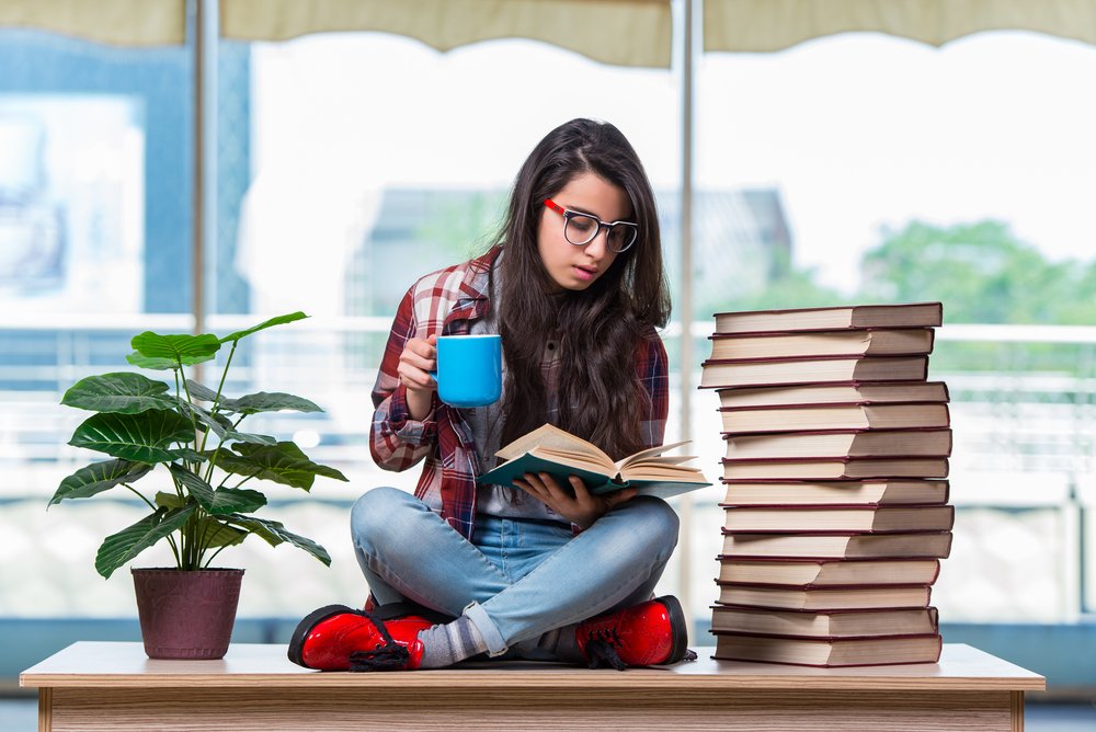 A nursing student reading a book and preparing for the TEAS exam surrounded by a stack of study books